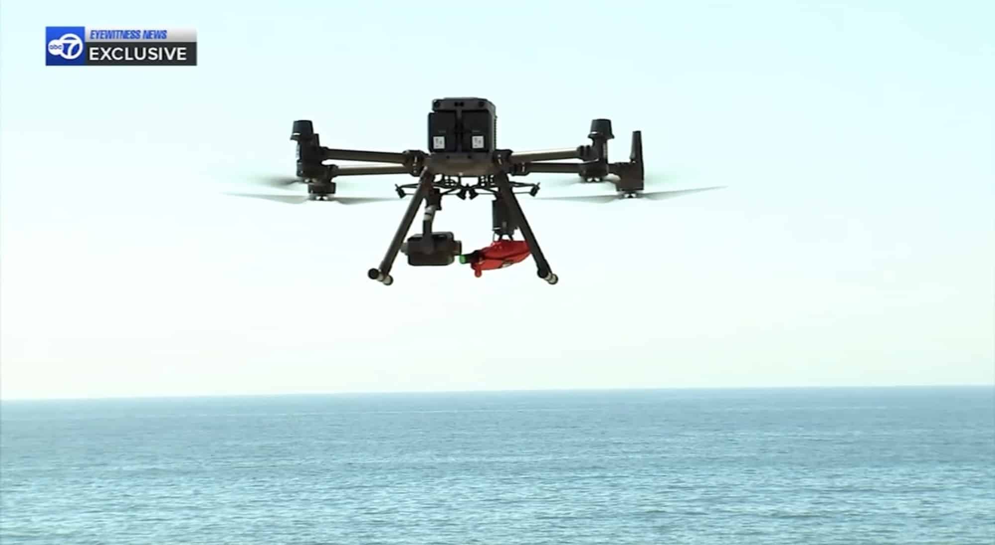 Matrice hovering high over the Atlantic surf carrying a red flotation pack.