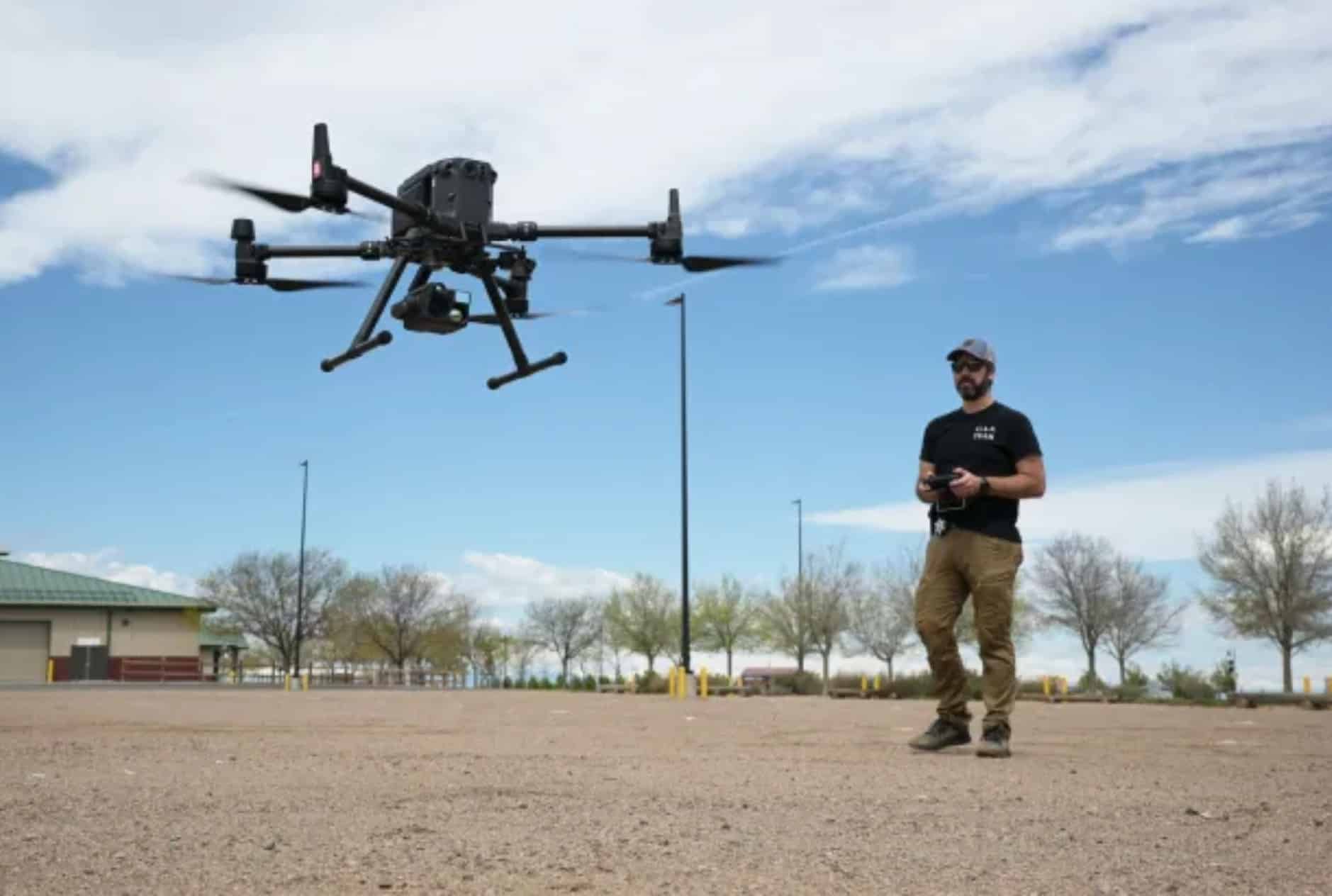 Officer flying a large enterprise quadcopter over a gravel lot on a clear day.
