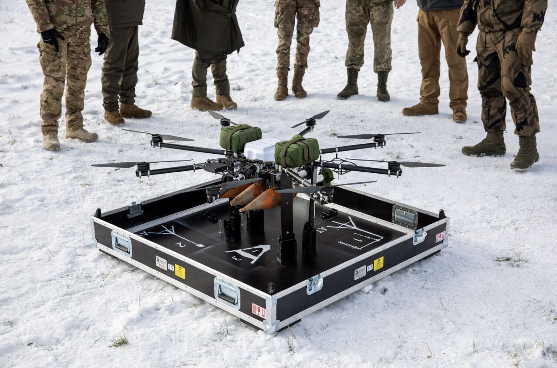 Heavy-lift multirotor loaded on a flight case in the snow with soldiers behind.