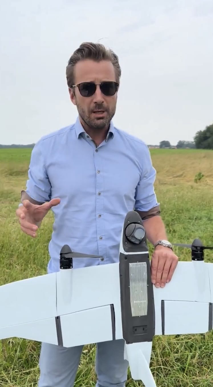 Florian Seibel holding up a smaller Quantum-Systems VTOL drone while speaking outdoors.