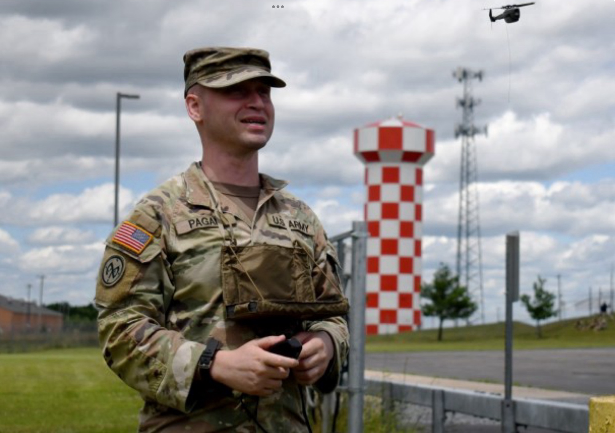 National Guard soldier flying a small drone beside a checkered airfield control tower.