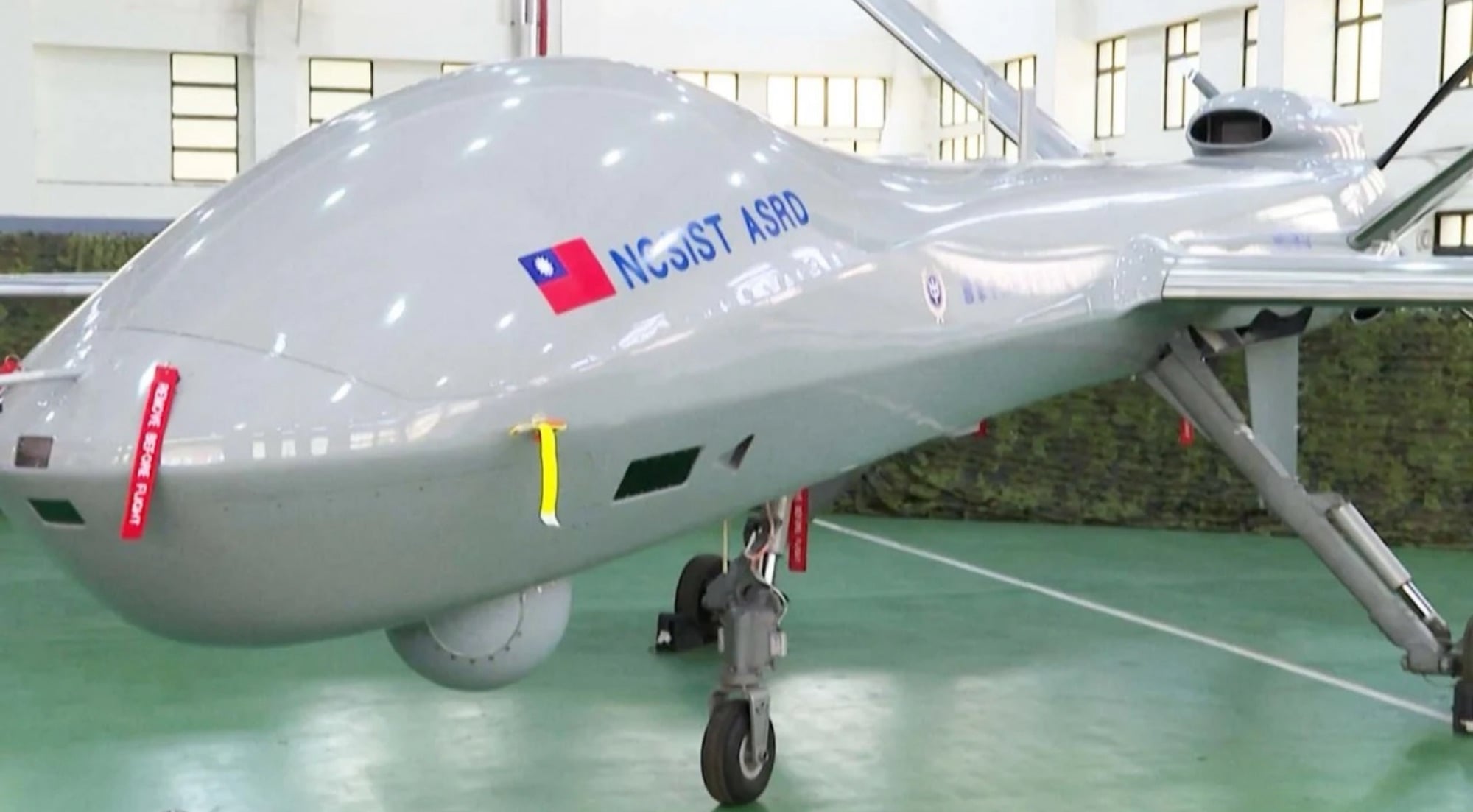 Gray unmanned aircraft marked NCSIST ASRD with a Taiwanese flag inside a hangar.