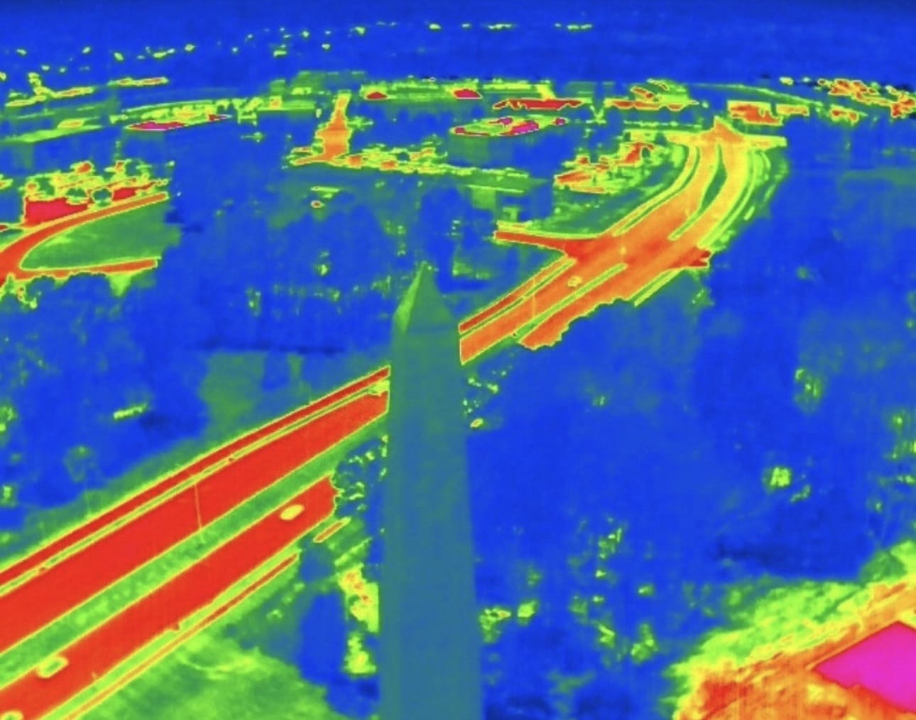 Thermal aerial frame showing hot roads and rooftops around a tall stone obelisk.