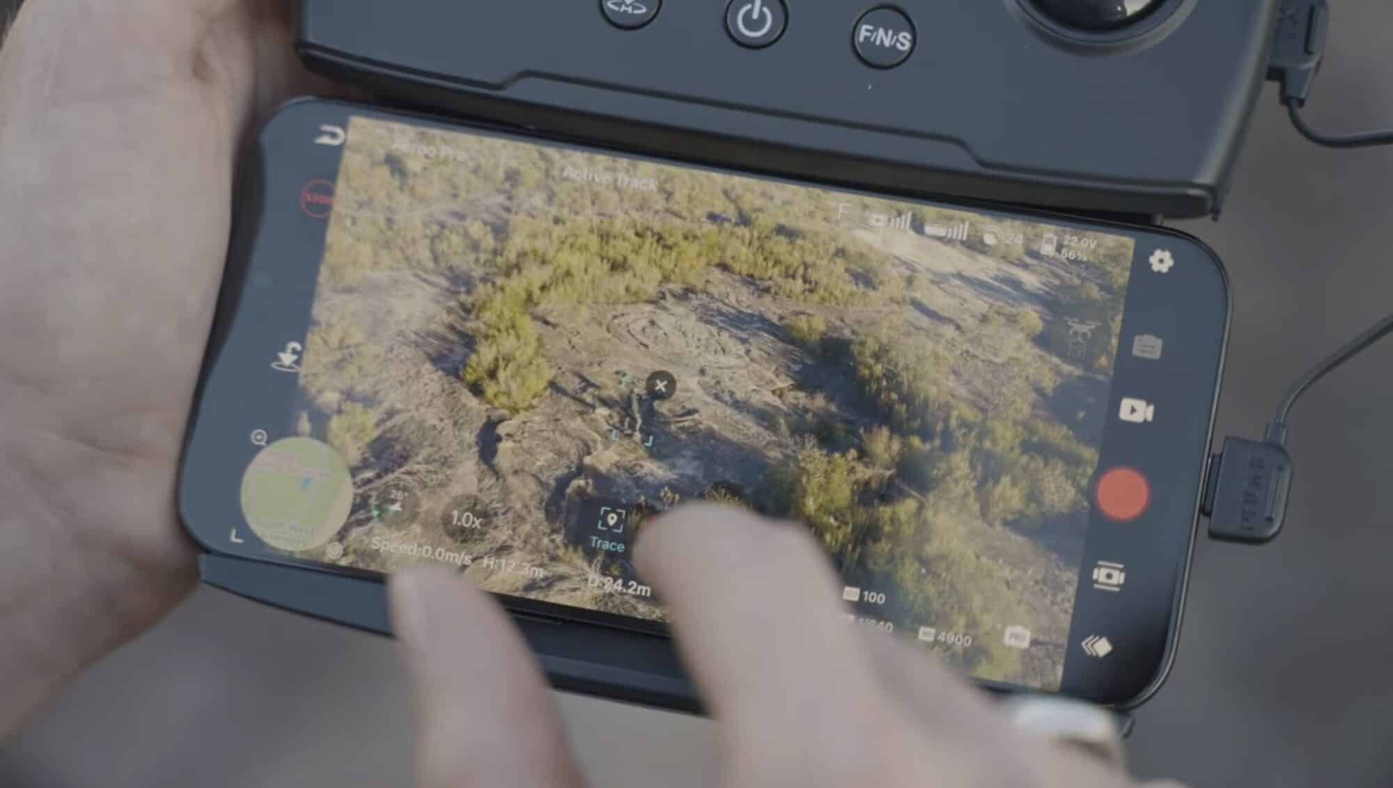 Pilot tapping the phone screen to track a subject over coastal scrubland.