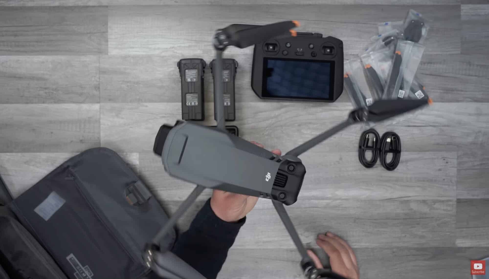 Overhead unboxing layout of a grey DJI Mavic with batteries, spare propellers and a controller.