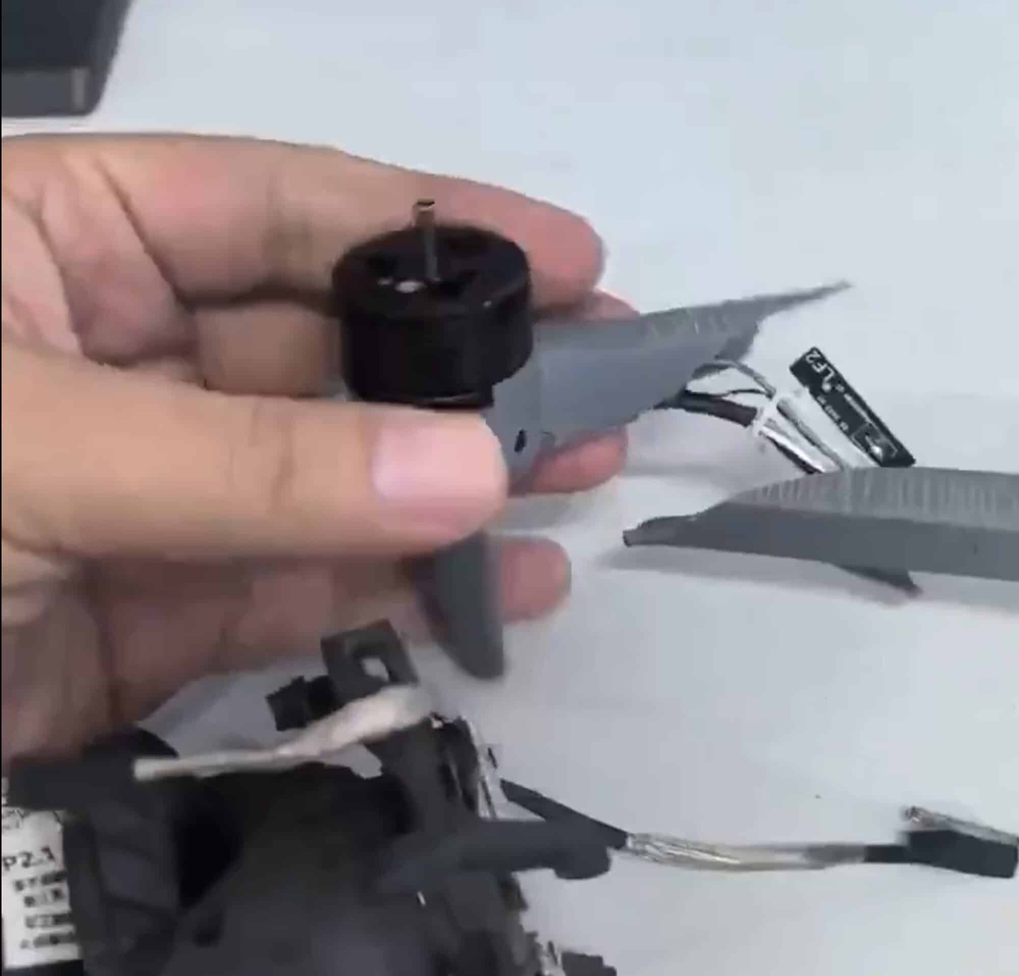 Hand holding the motor beside a gray propeller blade and stripped parts.