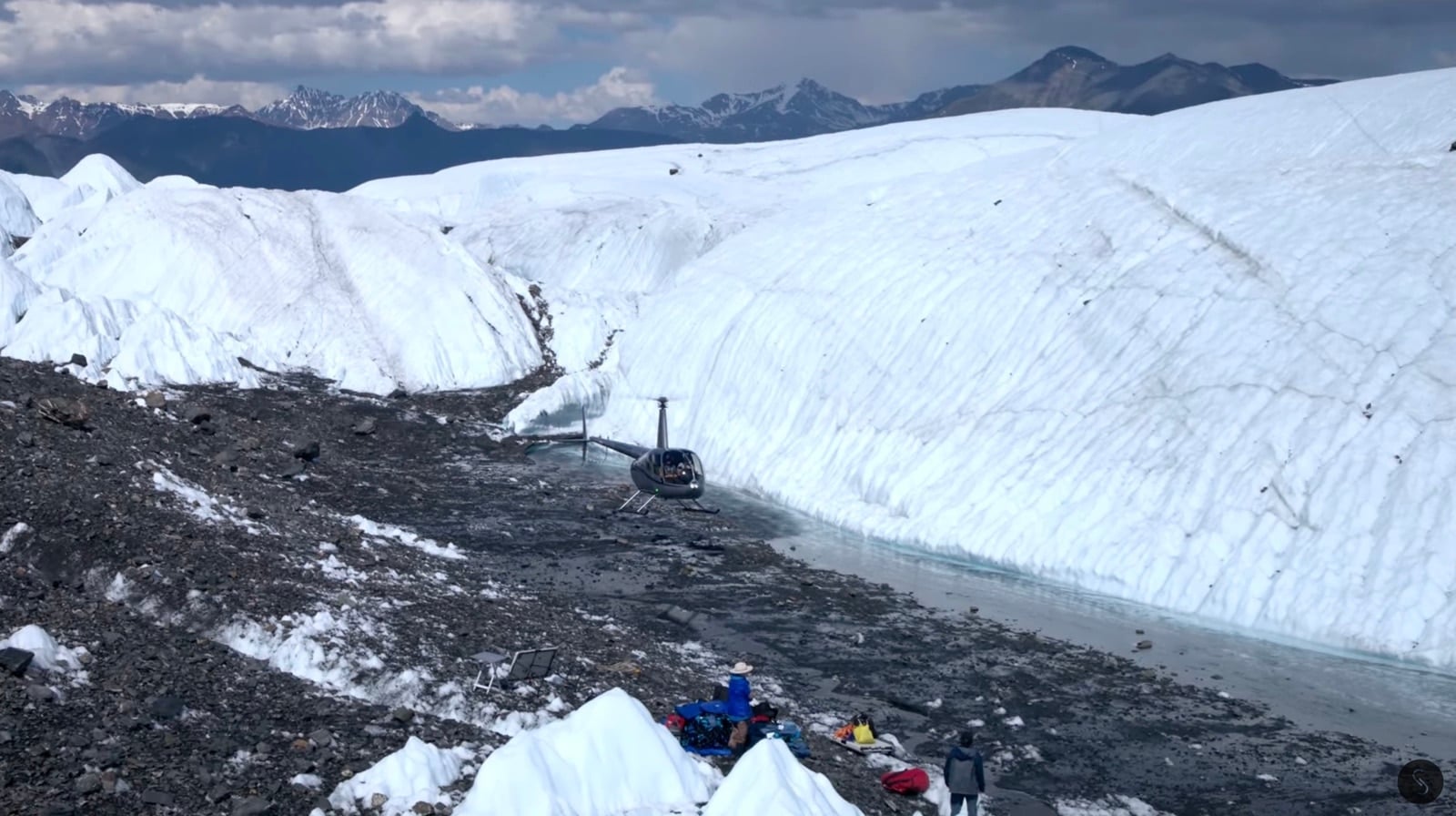 Helicopter parked on gravel beside the glacier ice face with gear and crew.