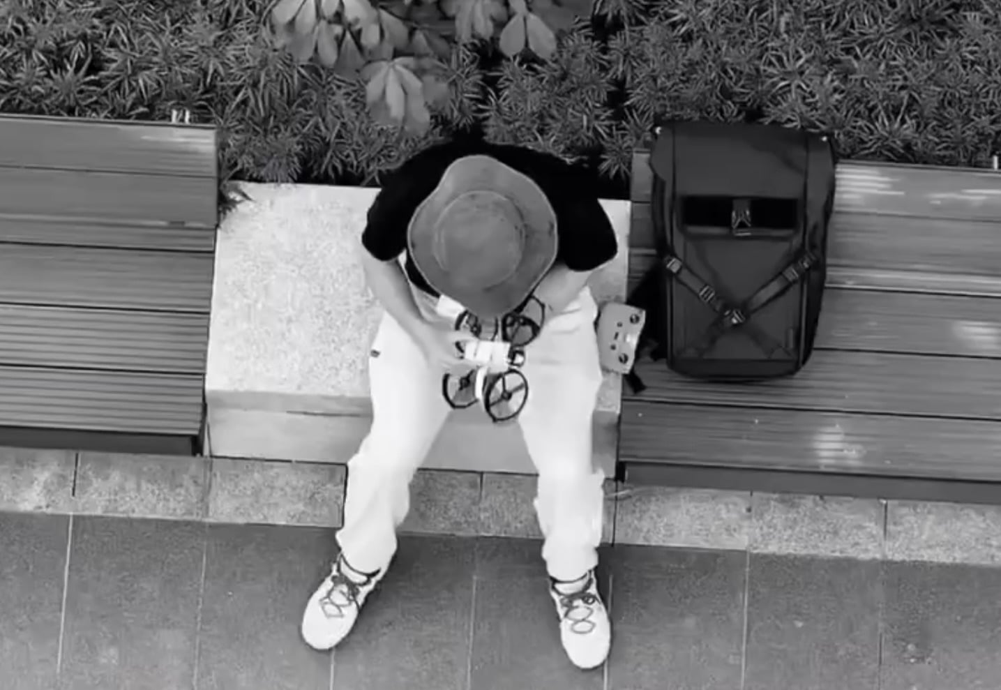 Overhead video frame of a DJI tester in a bucket hat seated on a bench.