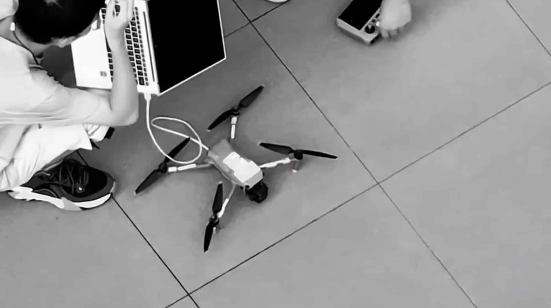 Tester crouched with a laptop cabled to a folding quadcopter on the paving.