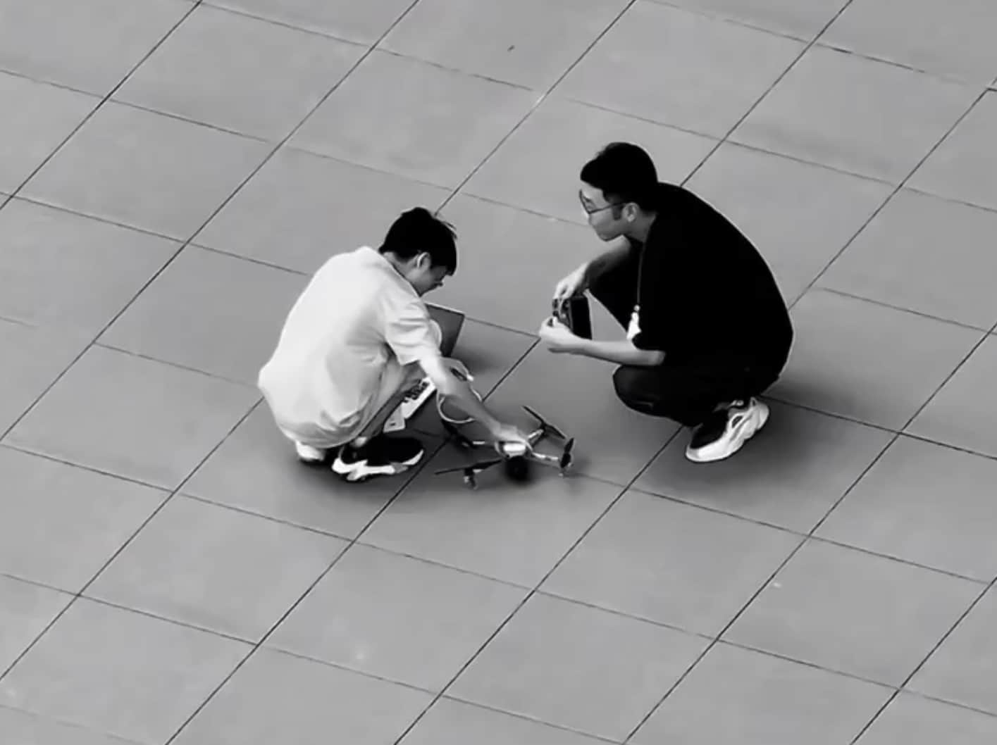 Two testers crouching over a folding drone on a paved plaza.