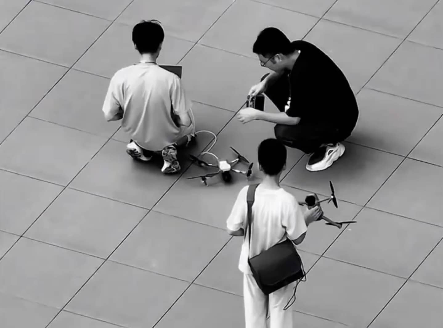 Three testers on the plaza, one carrying a second folding drone by hand.