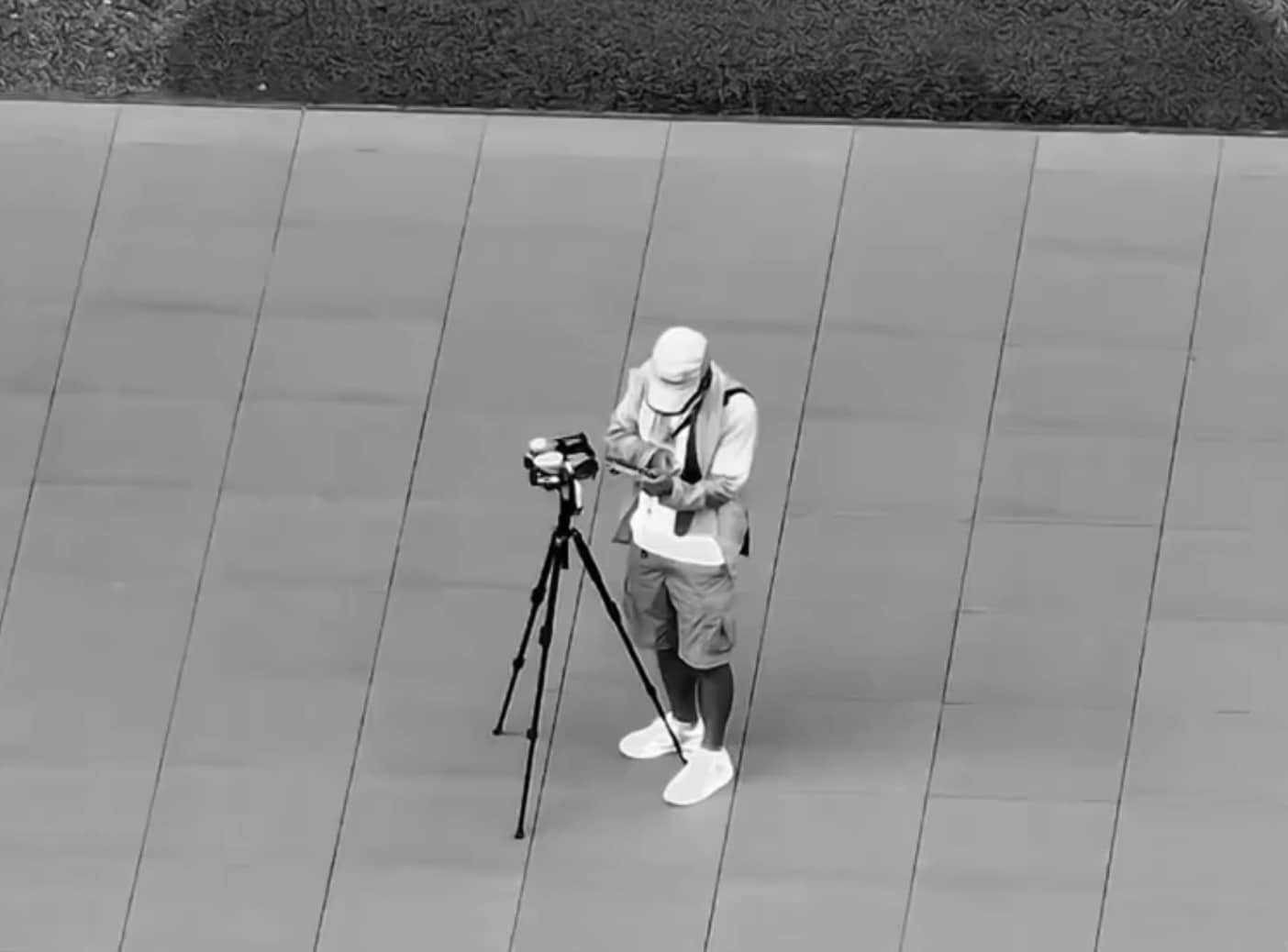 Tester in a bucket hat standing beside a tripod-mounted camera on the plaza.