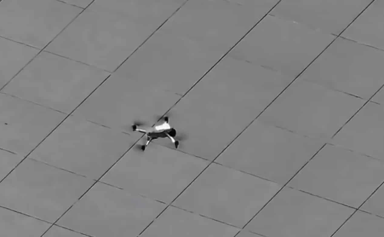 Folding quadcopter hovering a few feet above the paving, filmed from above.