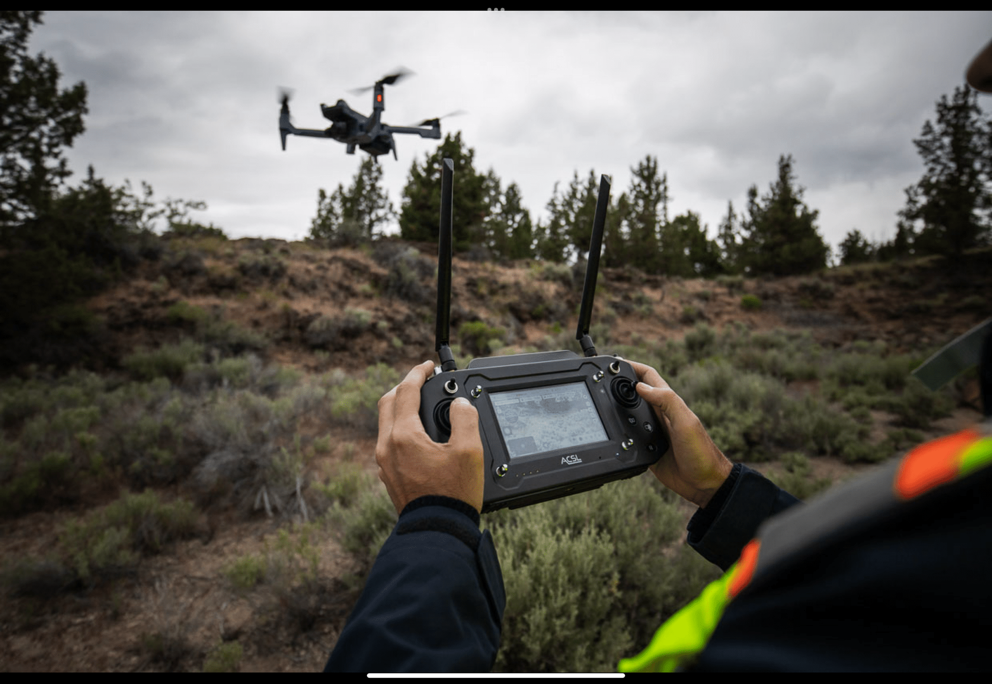Pilot flying the ACSL SOTEN quadcopter over sagebrush using the TENSO controller.
