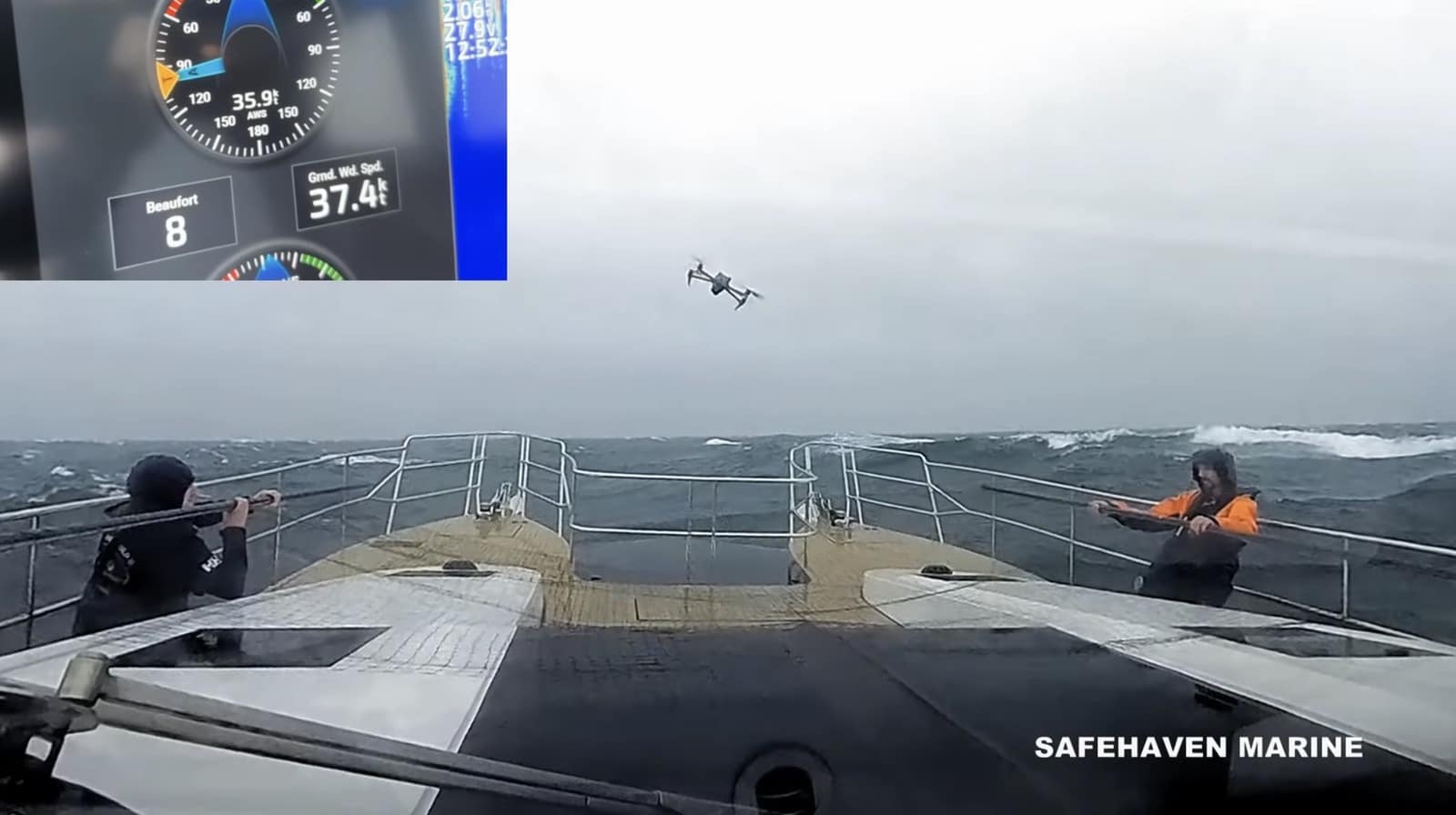 Two crew hold a net on the foredeck as the drone approaches in Beaufort 8 winds.