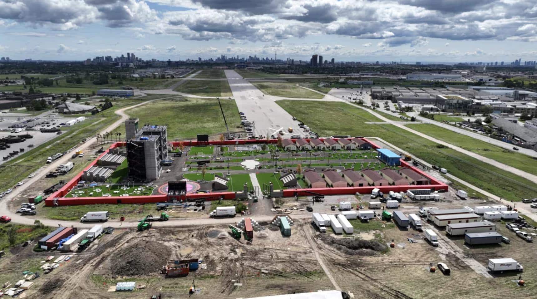 Wide aerial of the red-walled compound beside a runway with the Toronto skyline behind.