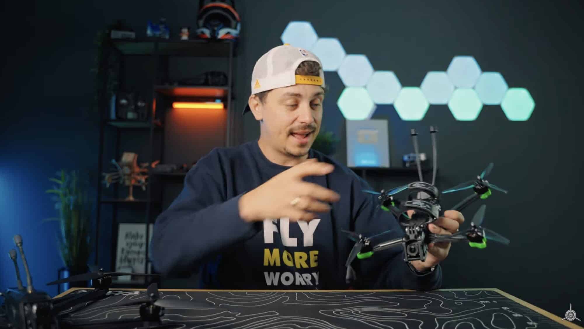 Creator at a desk holding a five-inch FPV freestyle quad in front of hex lights.