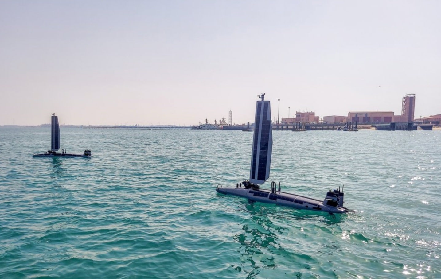 Pair of sea drones cruising near a naval pier in calm green water.