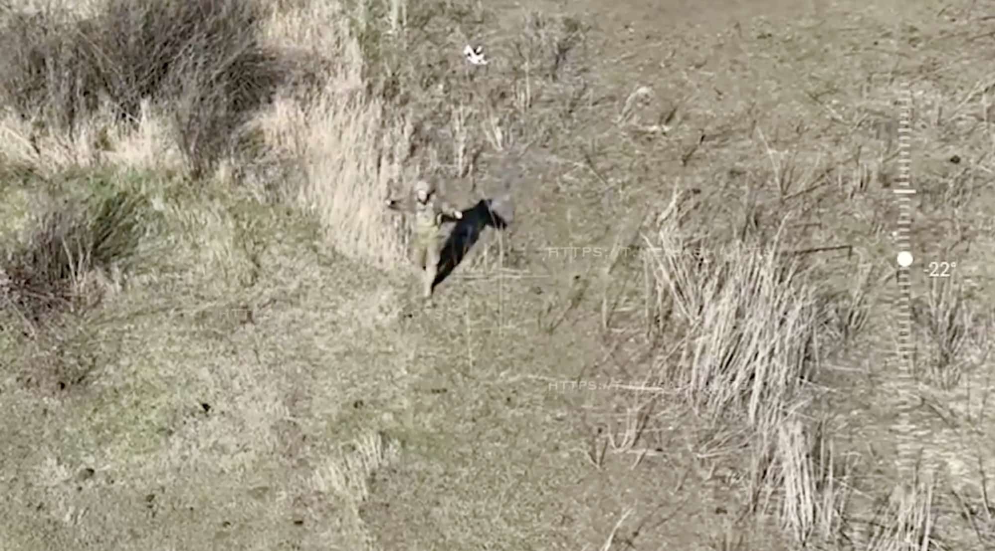Drone view of a lone figure moving through dry brush on a bare hillside.