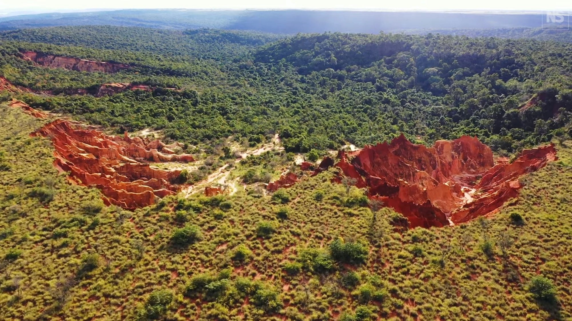 Aerial view of red erosion gullies biting into green Madagascar woodland.