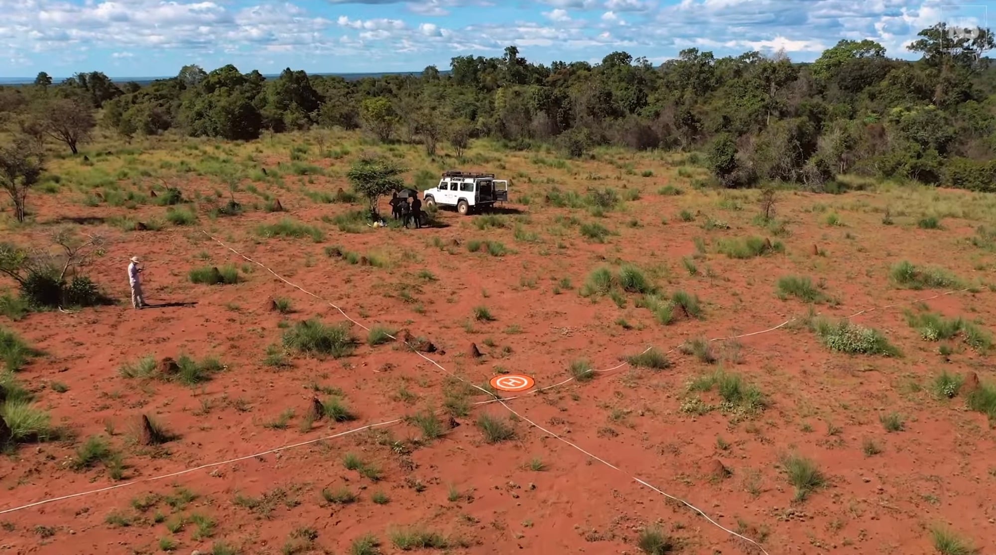 Aerial view of a landing pad and vehicle on a red laterite clearing.