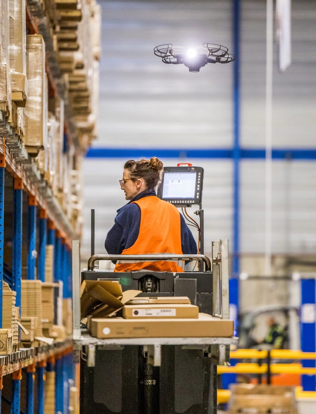 Inventory drone flying past warehouse racking as a worker rides an order picker.