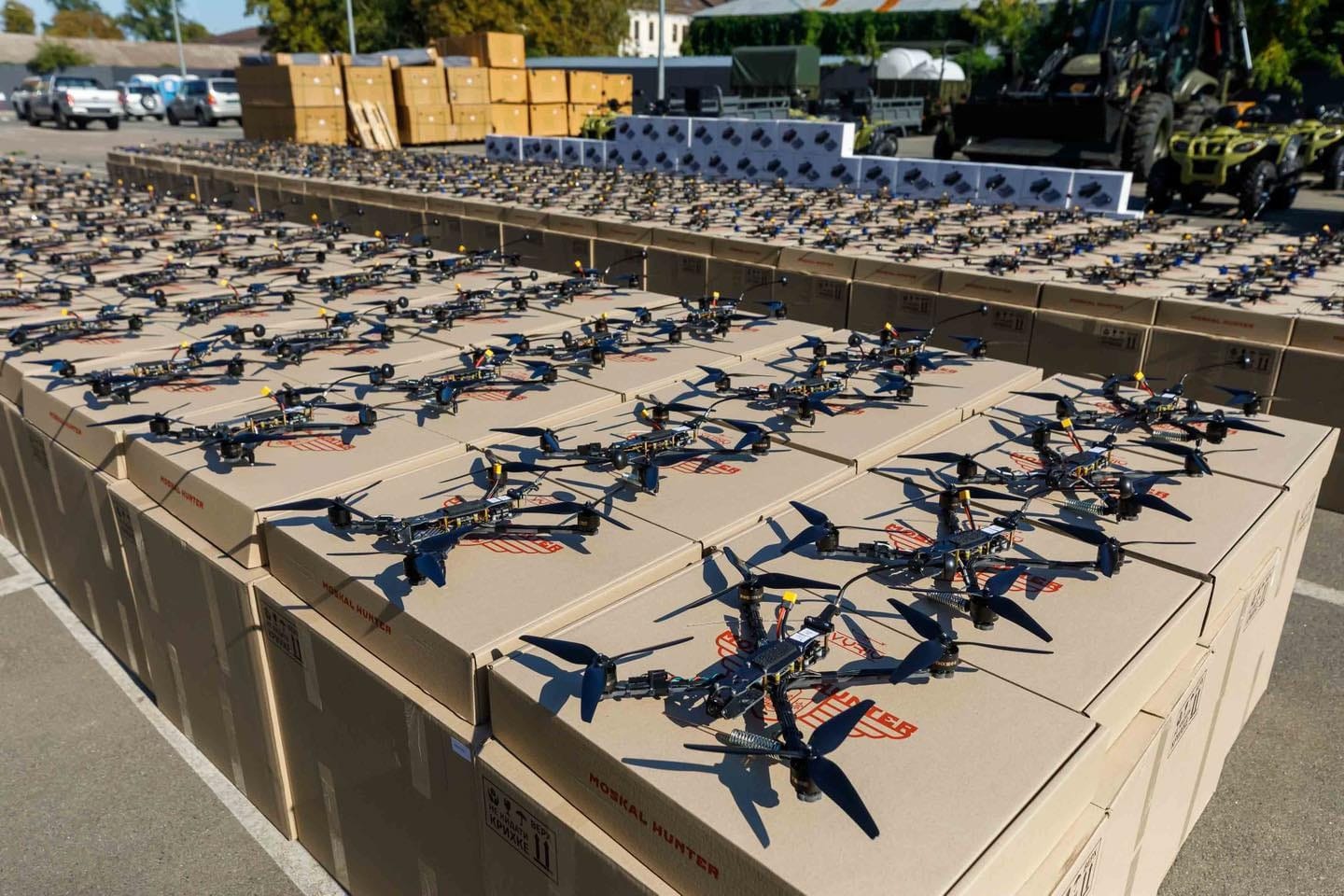 Hundreds of assembled FPV attack drones lined up across stacked cardboard shipping boxes.