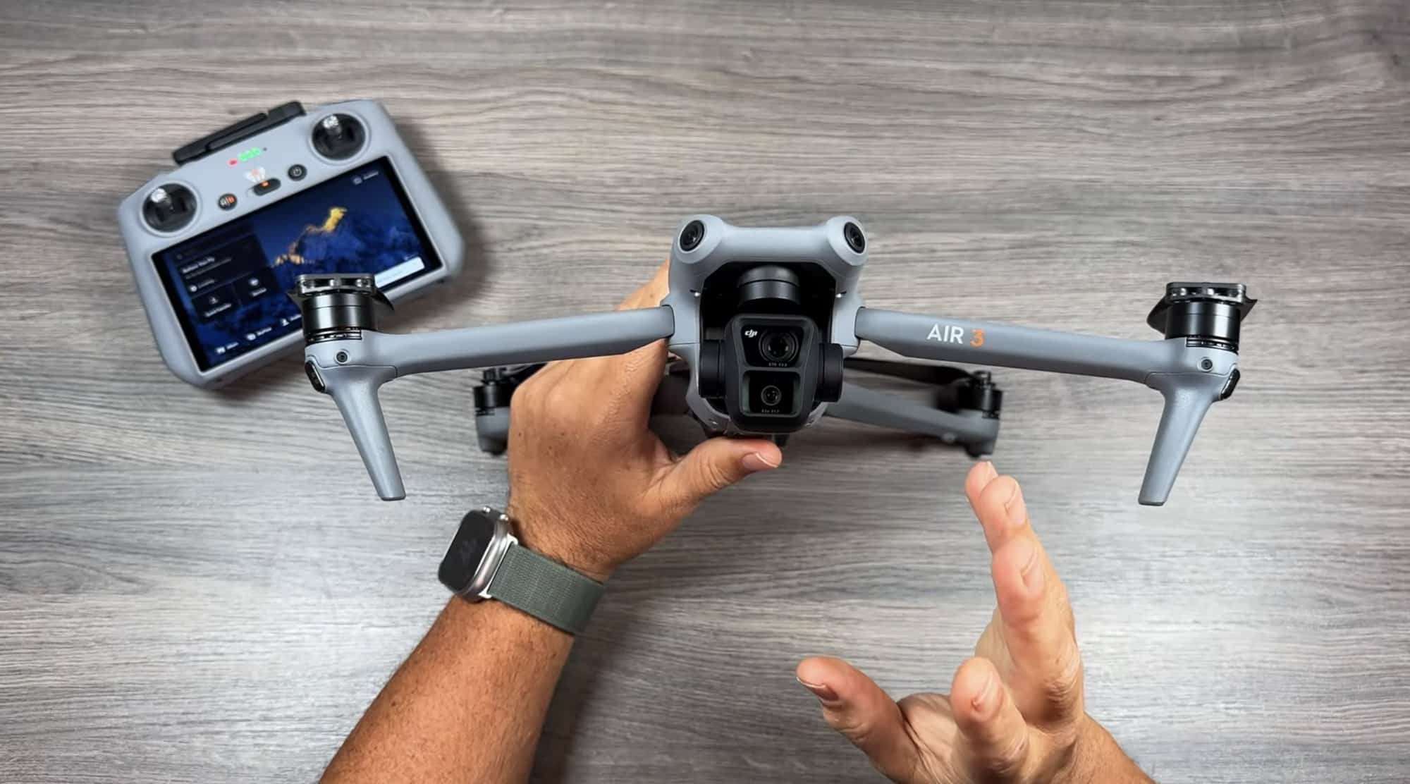 Hands unfolding a DJI Air 3 on a wood table beside its RC 2 controller.
