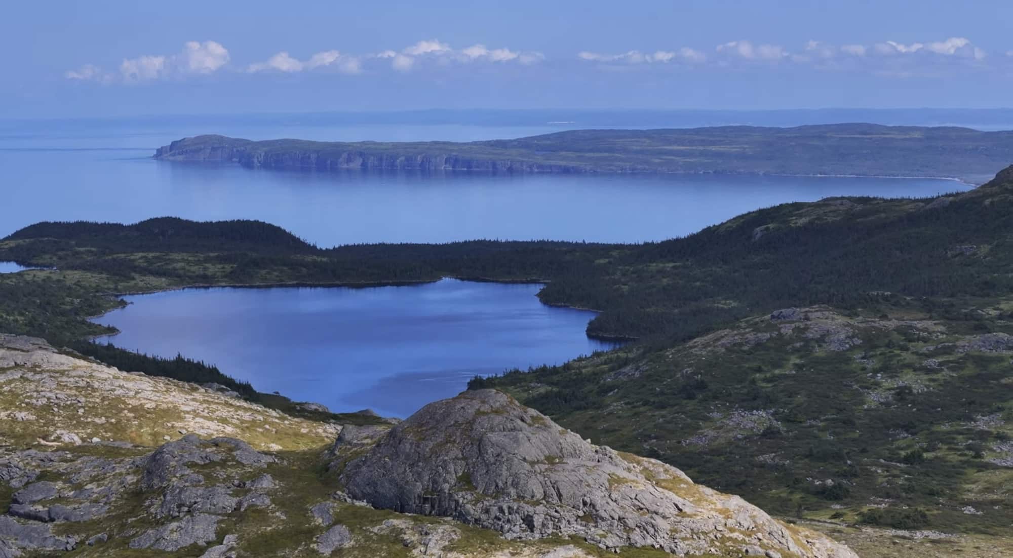 Aerial view of a blue inland pond ringed by rocky barrens above the sea.