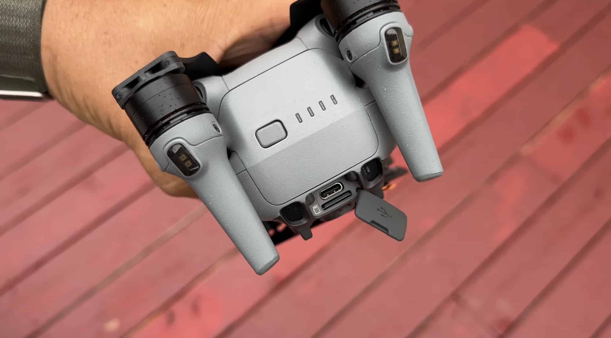Hand holding the folded Air 3 from below over red decking, ports exposed.