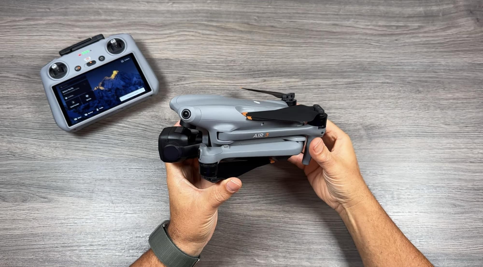 Hands holding the folded Air 3 with gimbal cover fitted, controller on the table.