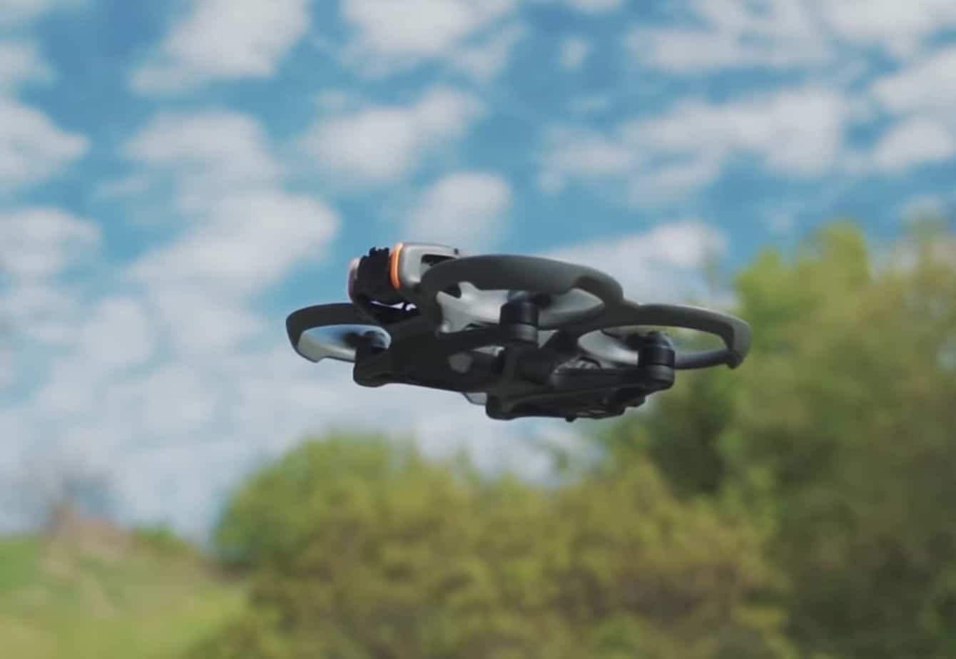 DJI Avata 2 hovering against a bright cloud-streaked sky above green treetops.
