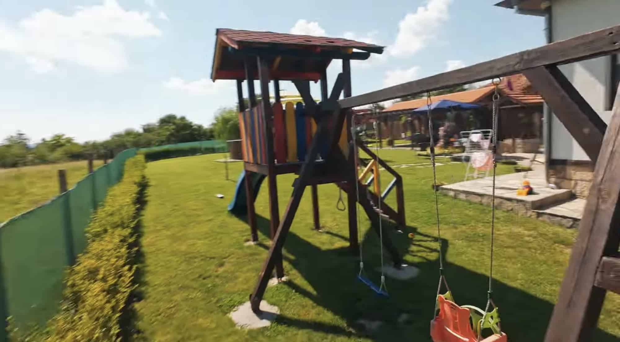 FPV flight past a backyard playhouse and swing set on a sunny day.