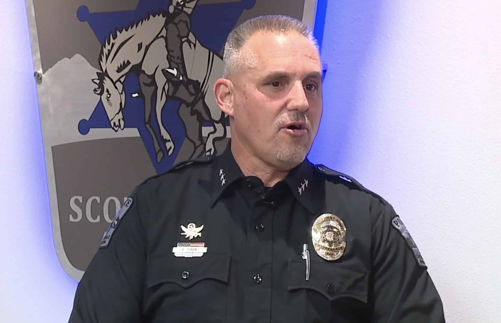 Scottsdale police commander speaking in front of the department crest during an interview.
