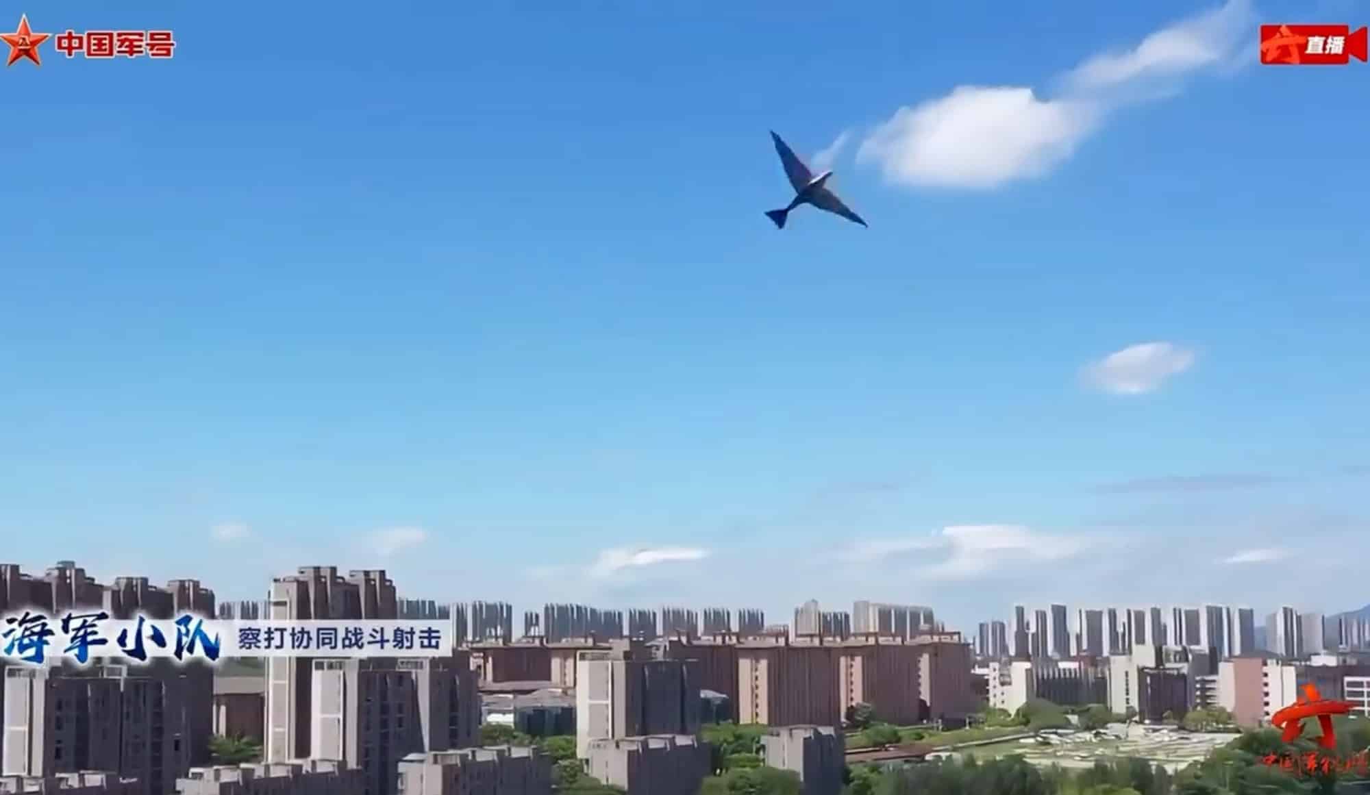 Bird-like ornithopter drone banking over a Chinese city skyline in military broadcast footage.