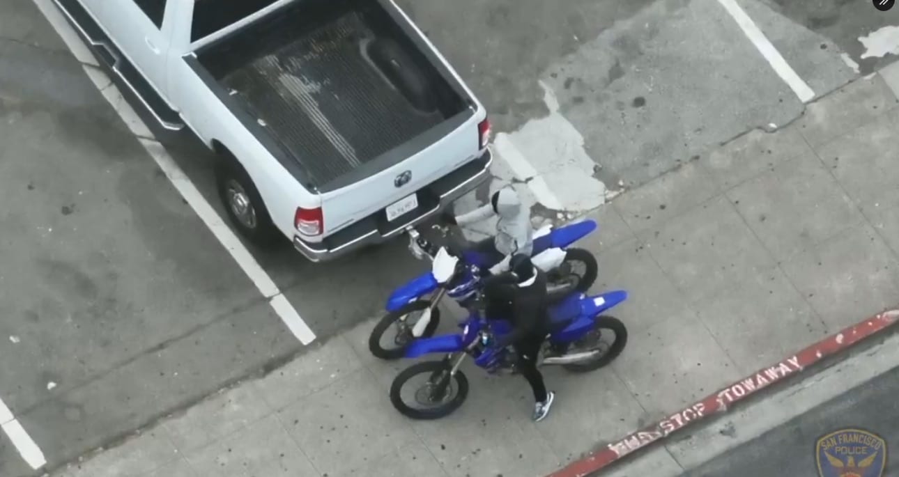 Police drone looking straight down at a blue dirt bike parked beside a pickup.