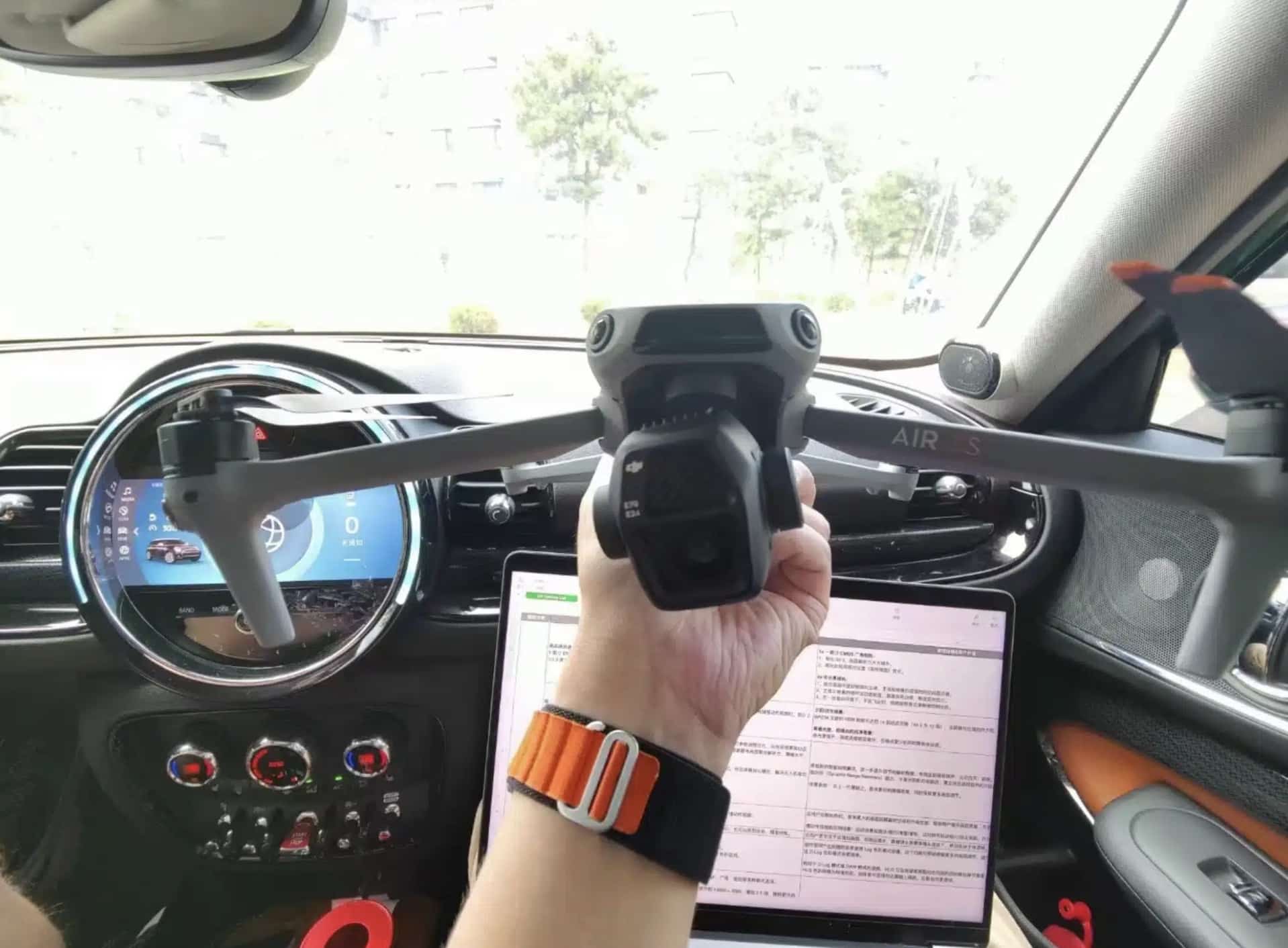 Hand holding the folded Air 3S inside a car beside the dashboard screen.