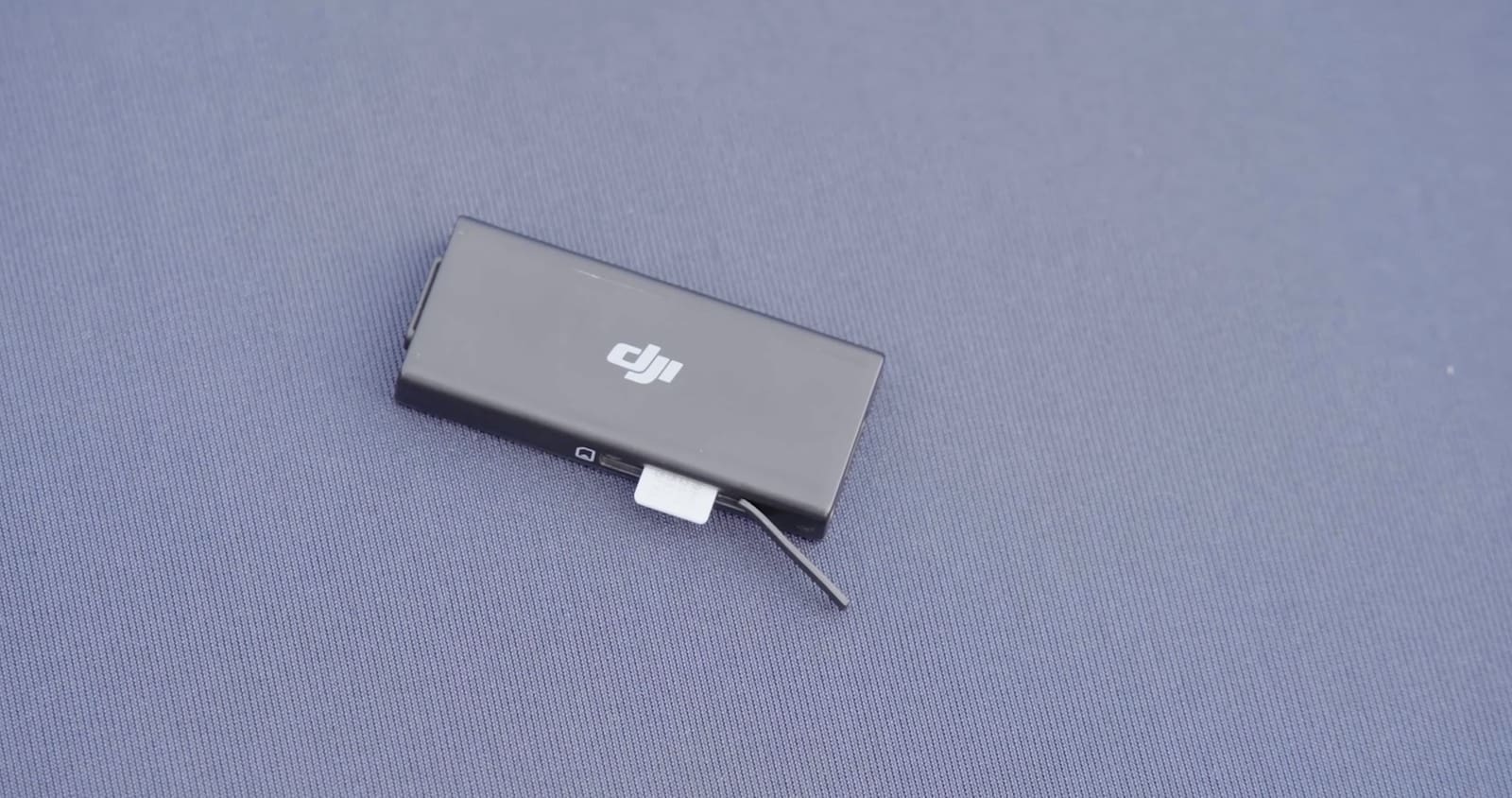 Close-up of the DJI Cellular Dongle and its short USB cable on blue fabric.