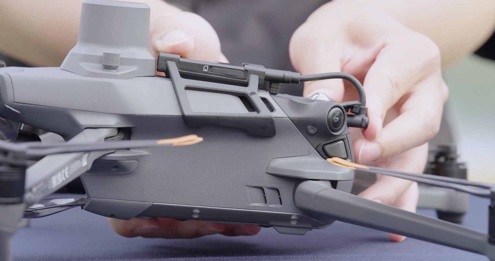 Fingers pressing the dongle connector into the port on the drone's side.