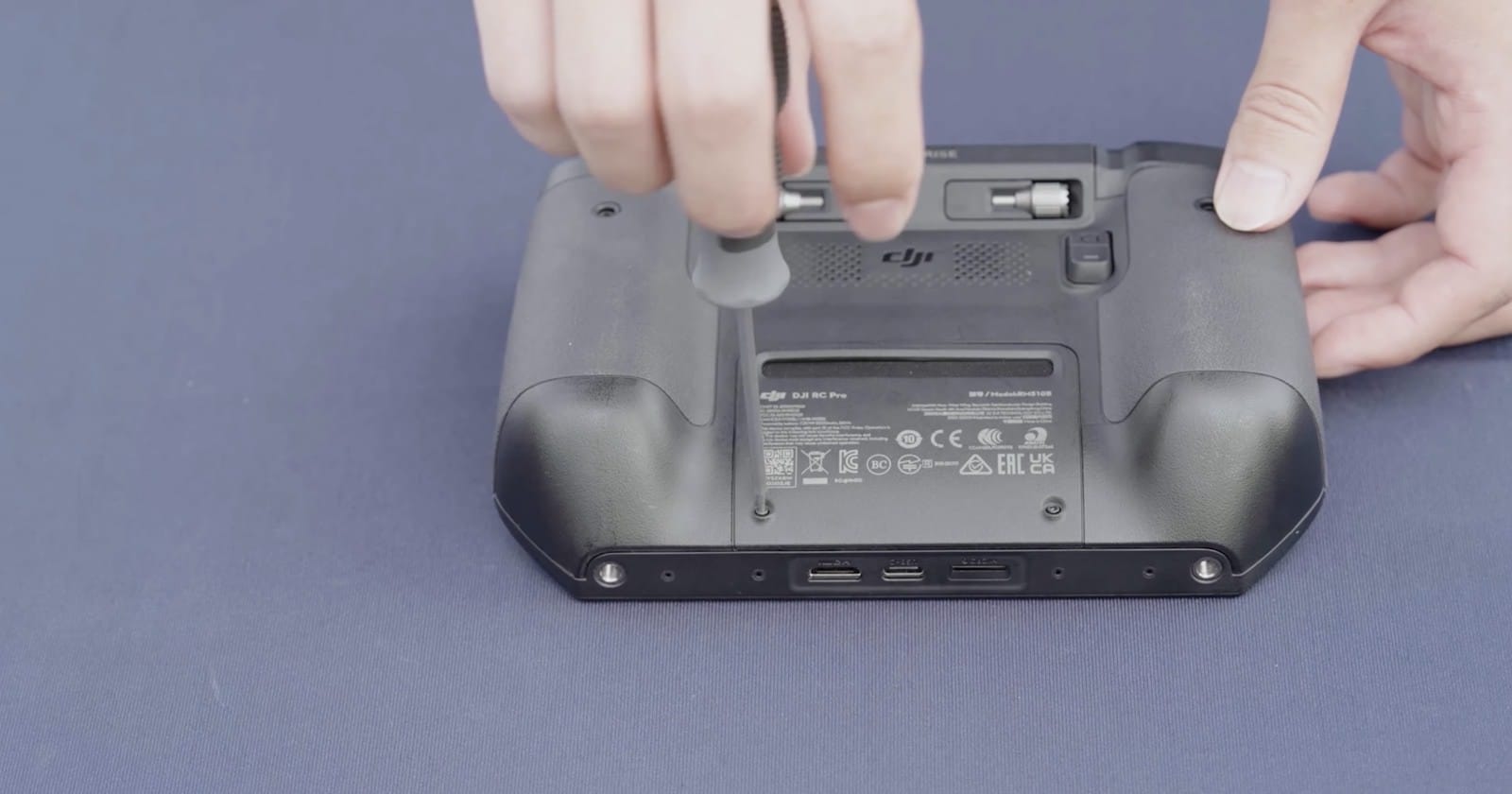 Hands loosening the thumbscrew on the back panel of the enterprise remote controller.