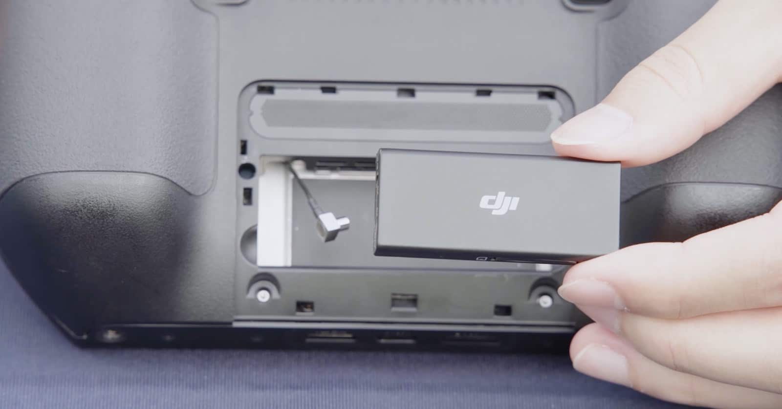 Hands sliding the DJI-branded dongle into the controller's rear compartment.