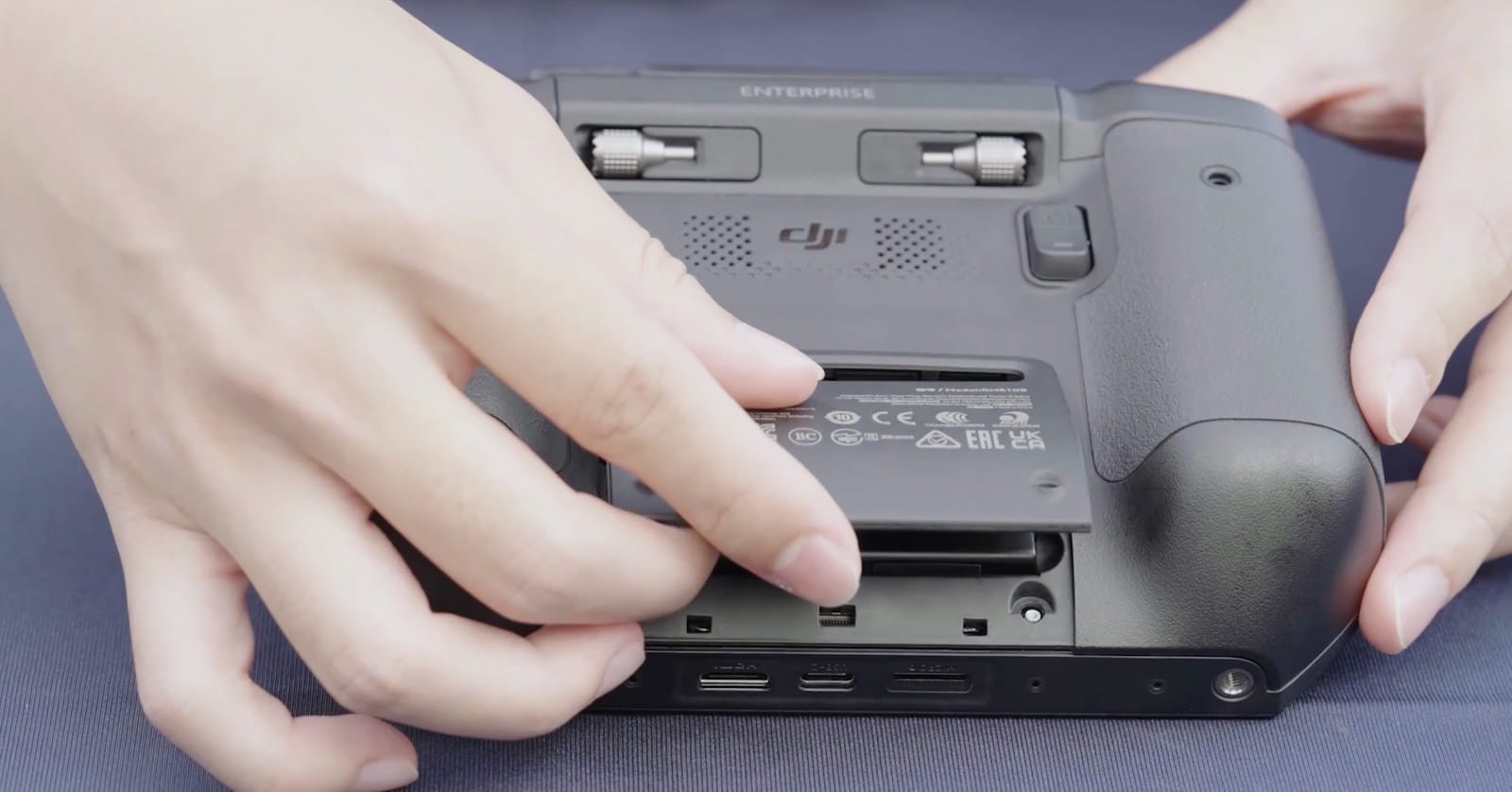 Fingers pressing the compartment cover shut on the underside of the controller.
