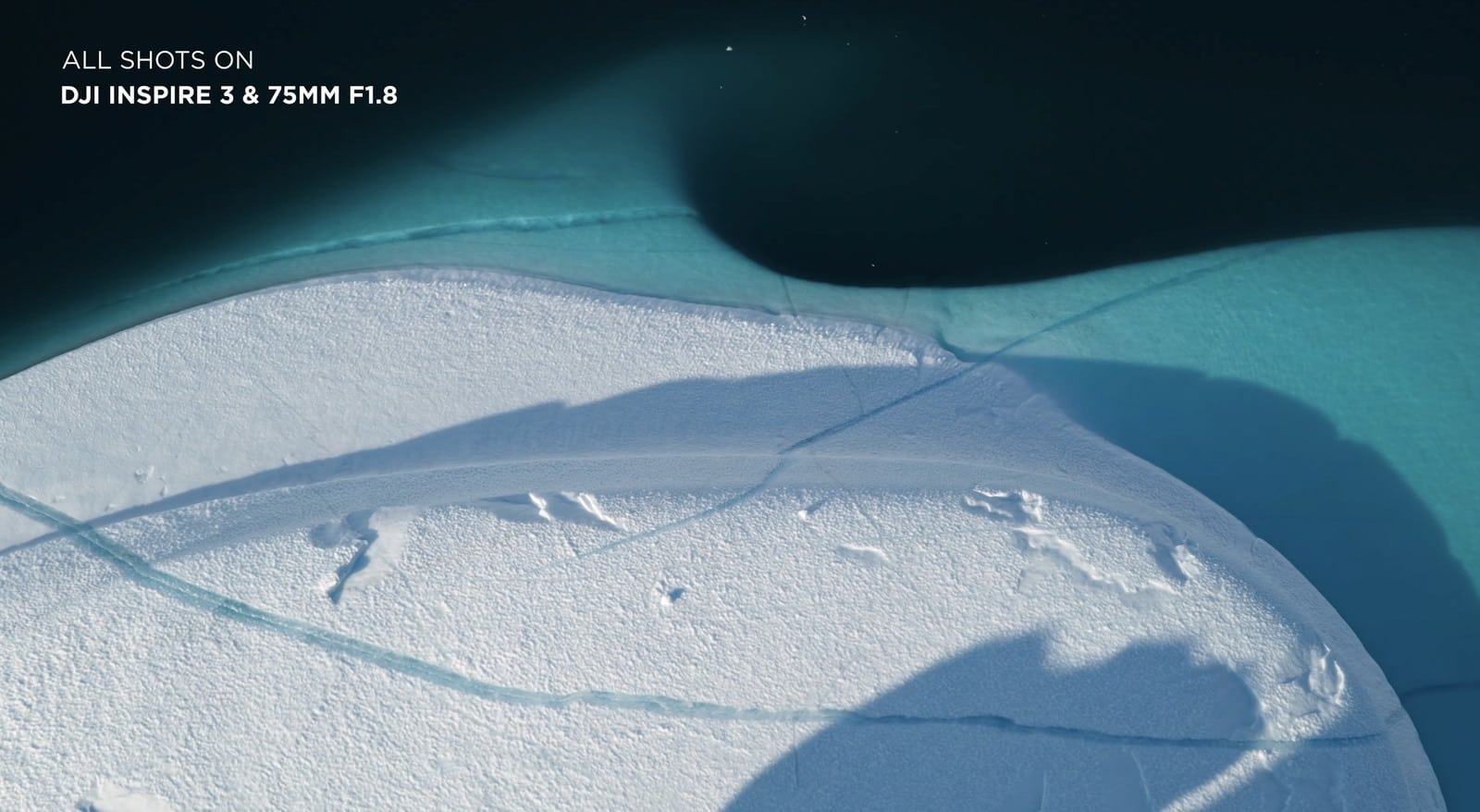 Aerial of a snow-covered ice edge meeting turquoise meltwater, captioned with the lens credit.