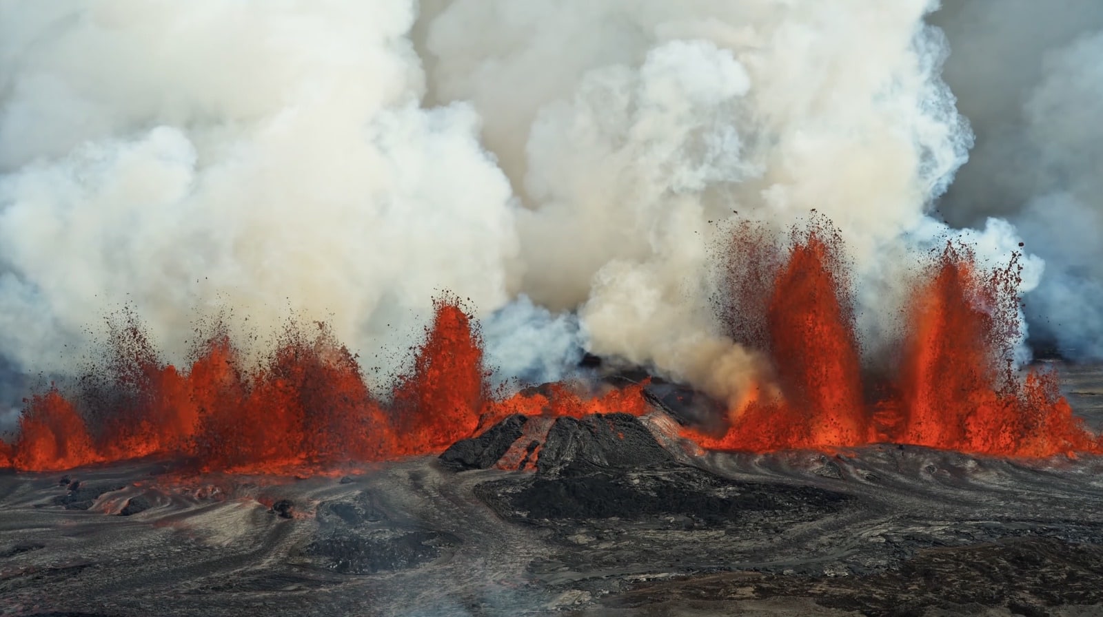 Lava fountains erupting along a fissure with white steam drifting over the crater.