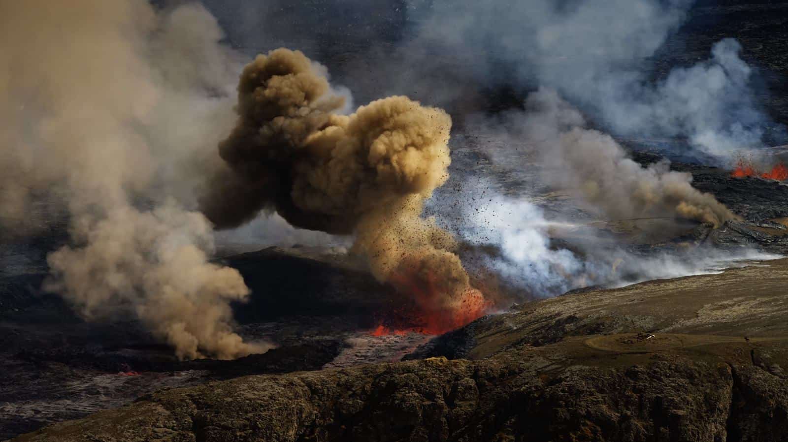 Dark ash plume boiling from a volcanic vent with glowing lava at its base.