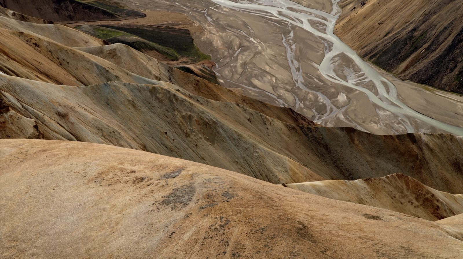 Compressed aerial of smooth rhyolite ridges beside a braided glacial river.