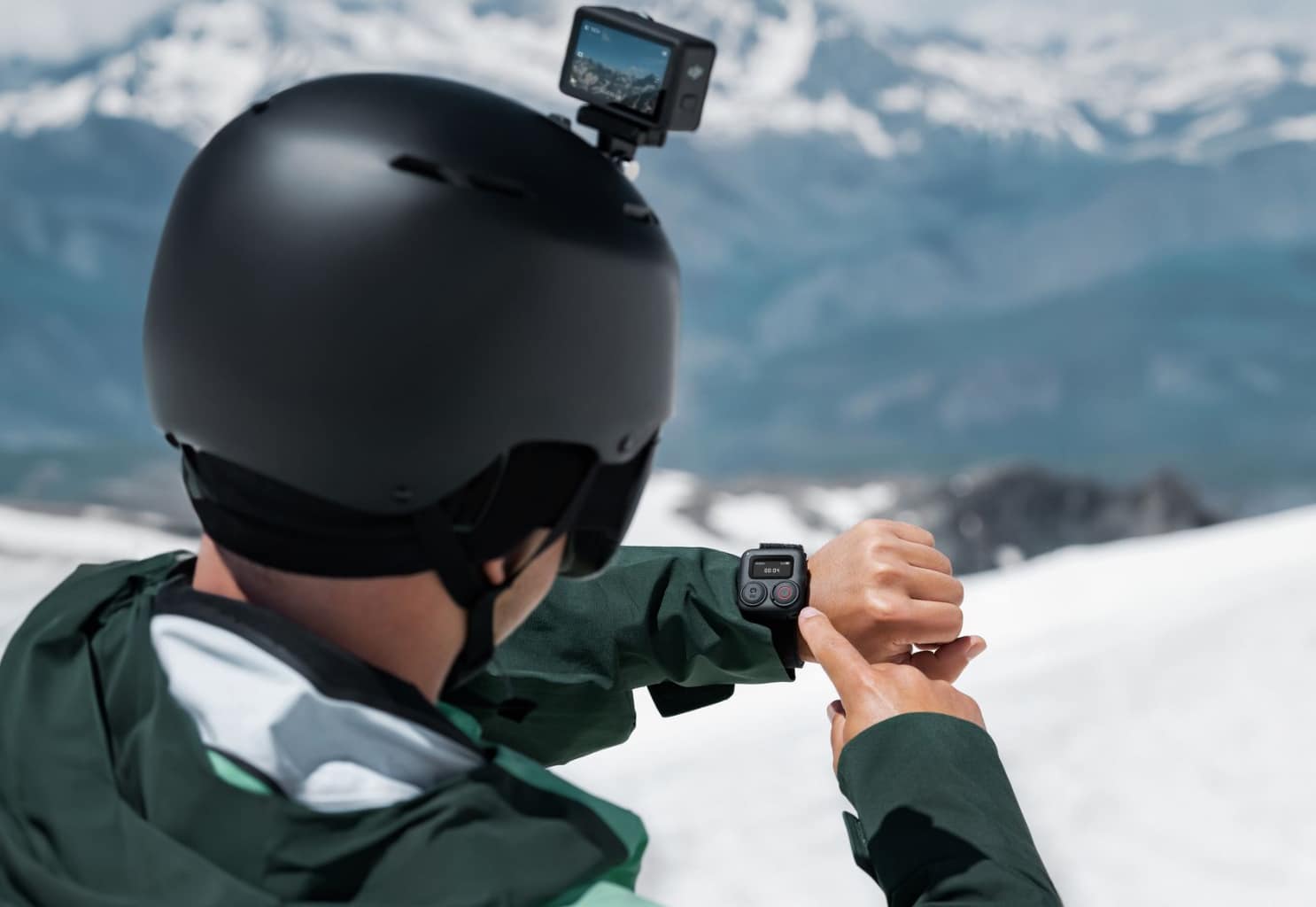 Skier in a black helmet checking the wrist-mounted Bluetooth remote in the mountains.