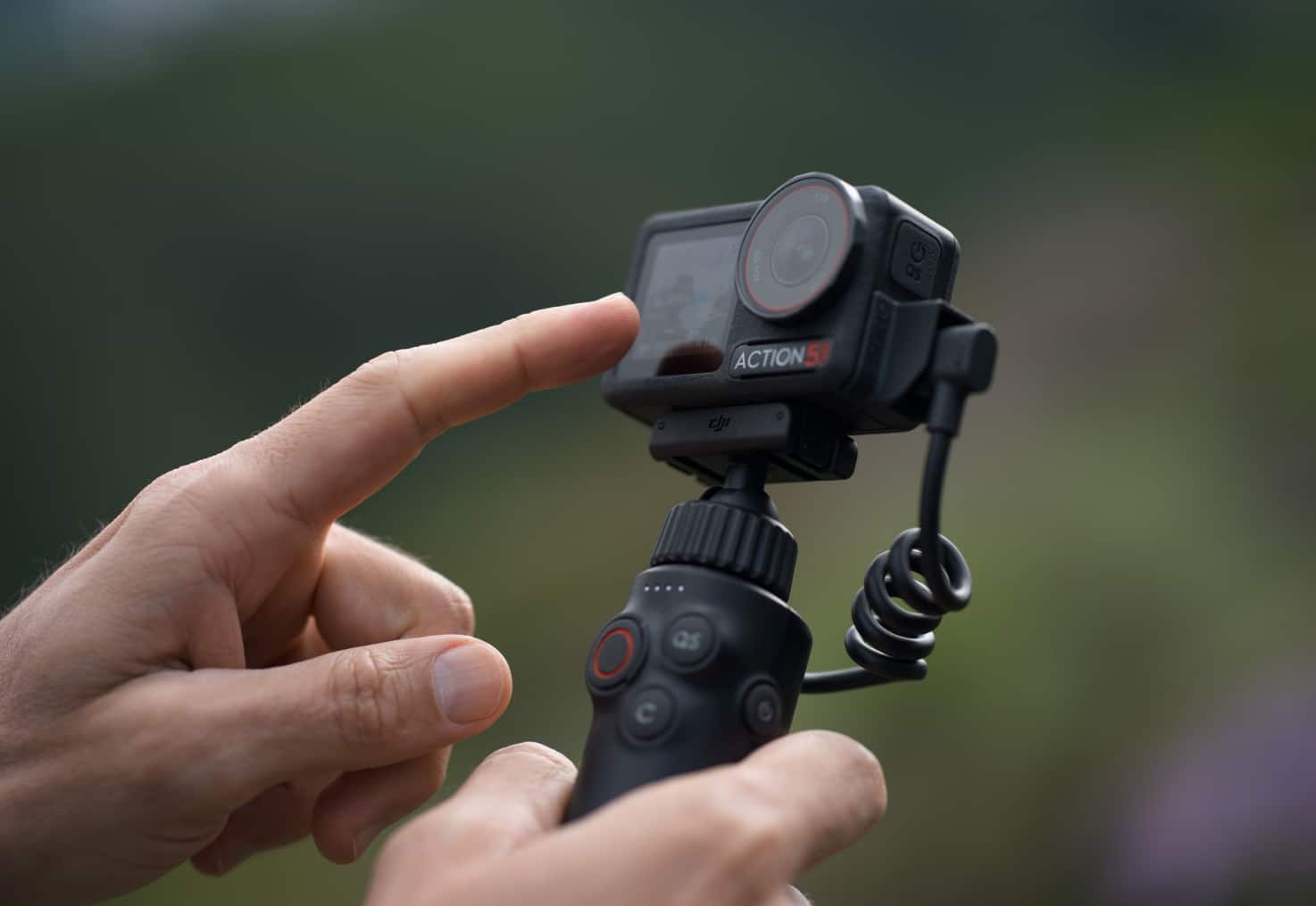 Finger tapping the Osmo Action 5 Pro mounted on the multifunctional charging handle.