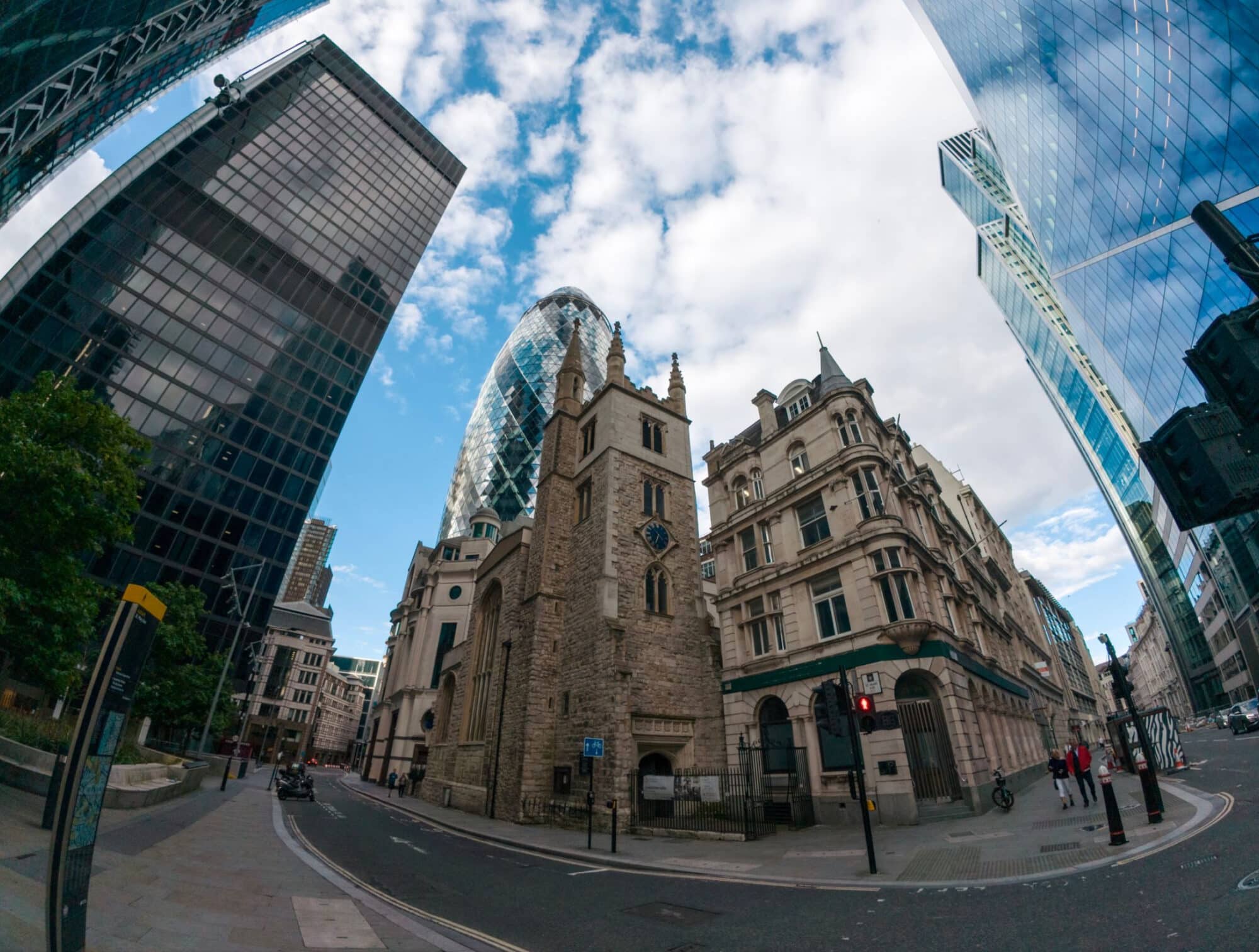 Ultra-wide street-level view of London office towers beside an old stone church.