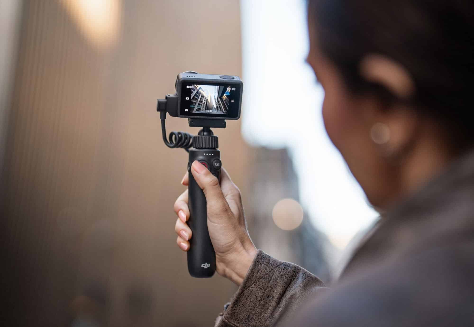 Woman holding an Osmo Action 5 Pro on a charging handle in a city street.